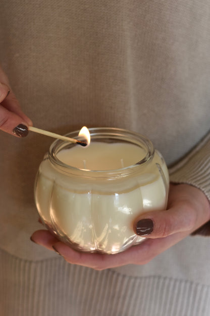 Person lighting a candle in a glass jar with a beige sweater background