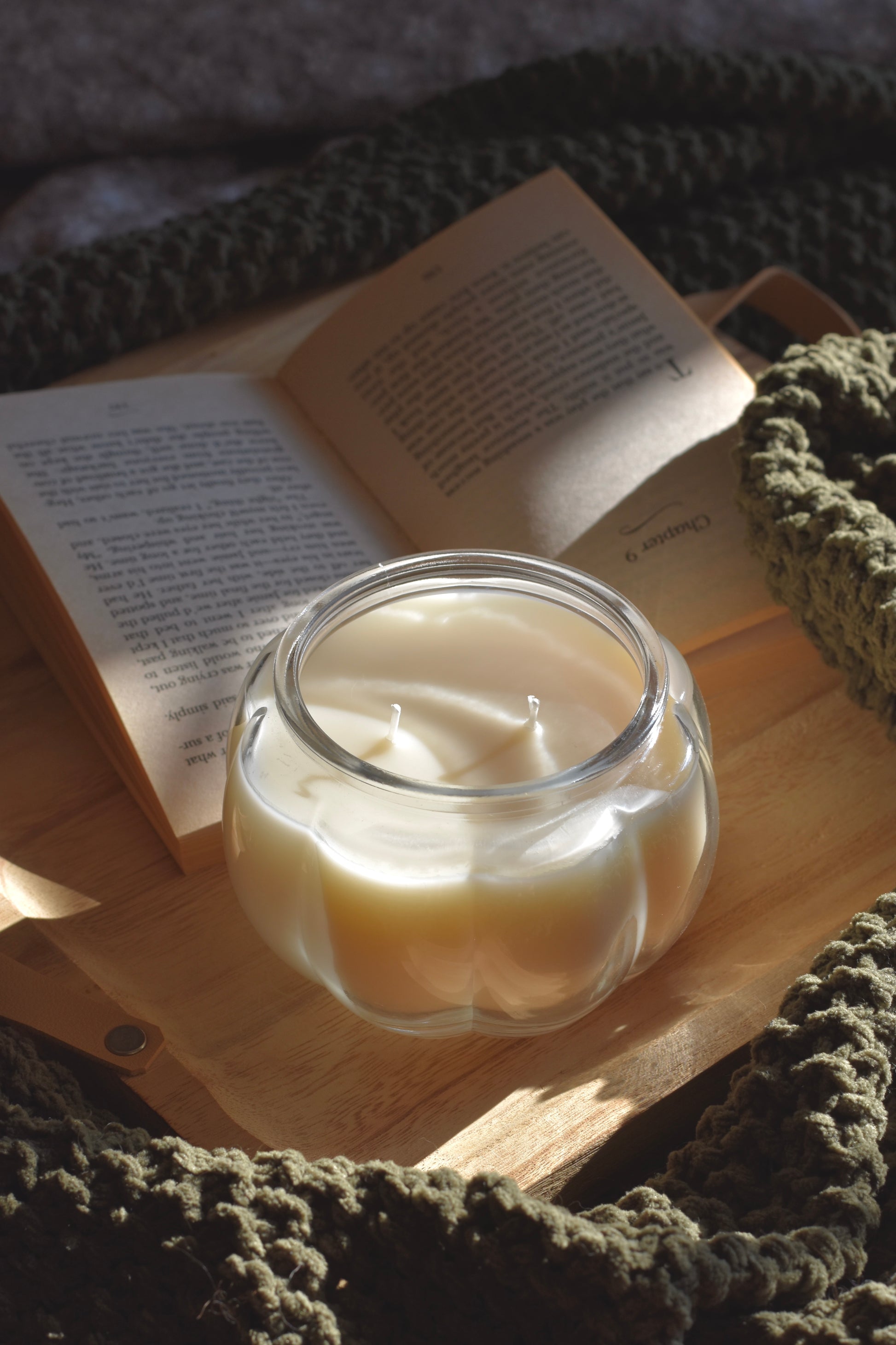 Candle in a glass jar with an open book on a wooden surface