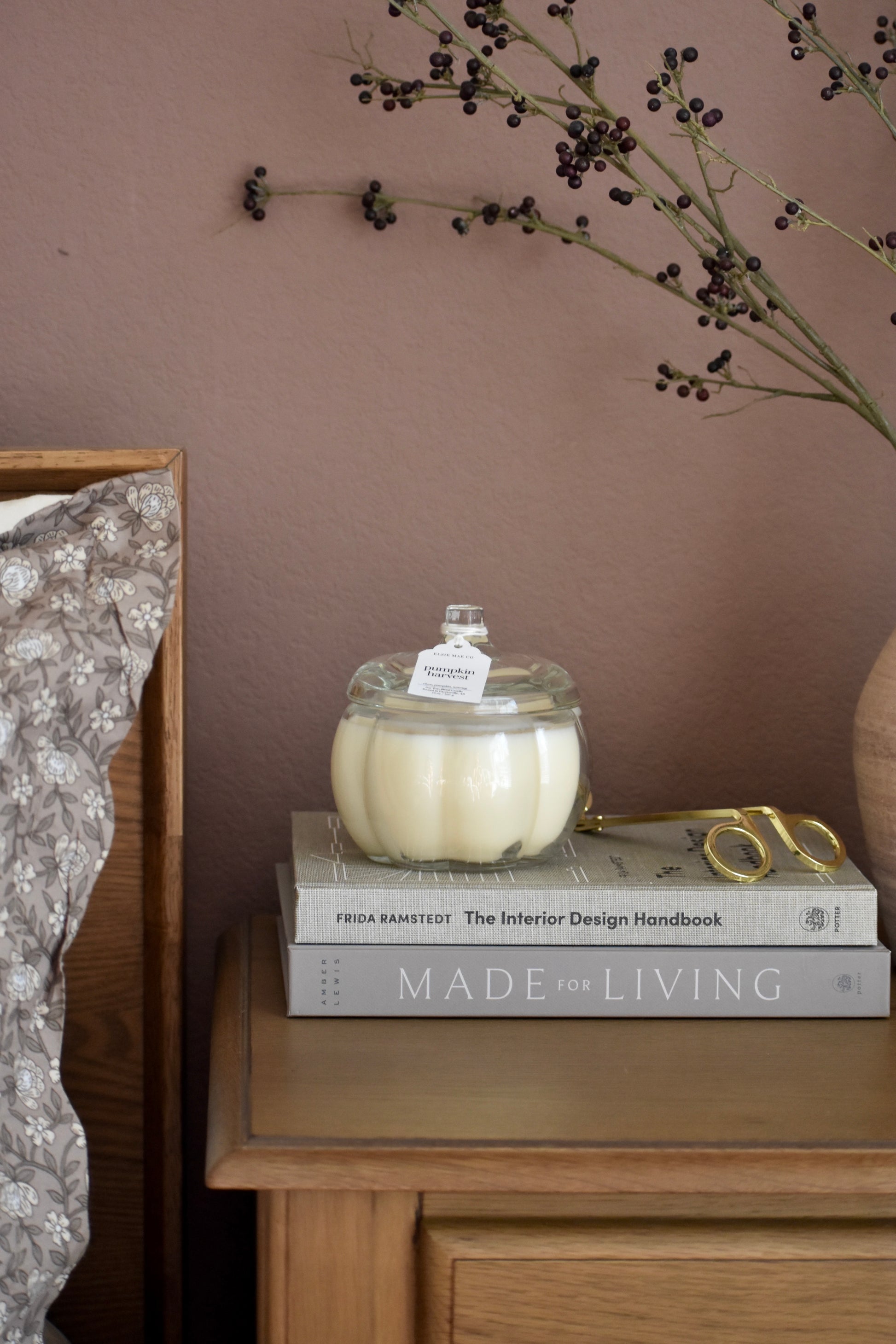 Candle in a glass lid on top of books with a decorative branch on a wooden surface.